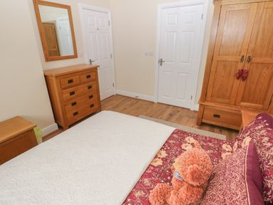 A bedroom with a bed, wooden dresser with mirror, wooden wardrobe, and two closed white doors at Llygad Yr Haul Sun in Burry Port