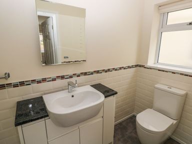 A bathroom with a sink and cabinet unit next to a toilet under a frosted window at Llygad Yr Haul Sun in Burry Port