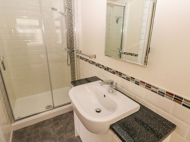 A bathroom with a shower enclosure a sink with black countertop and a mirror at Llygad Yr Haul Sun in Burry Port