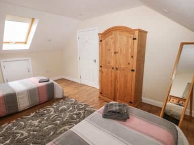 A bedroom with two single beds towels a wooden wardrobe a full length mirror and a skylight window at Llygad Yr Haul Sun in Burry Port