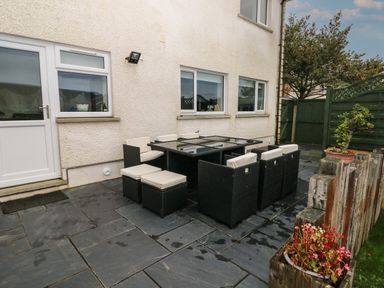An outdoor patio area with a black glass table and wicker chairs with cushions at Llygad Yr Haul Sun in Burry Port