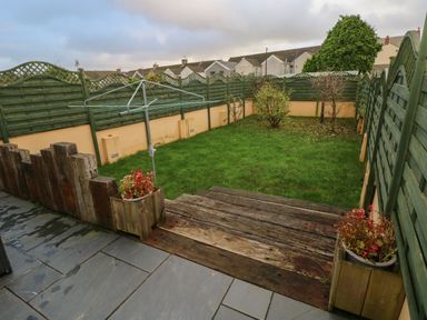 A fenced backyard with a grass lawn a rotary clothesline wooden steps and flower pots at Llygad Yr Haul Sun in Burry Port