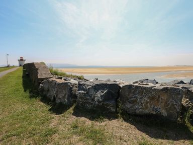 A coastal walkway with rocks and a small lighthouse near a sandy beach at Llygad Yr Haul Sun in Burry Port