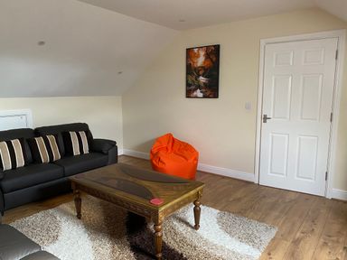 A sitting room with a black sofa and cushions a wooden coffee table an orange bean bag and a framed picture on the wall at Llygad Yr Haul (Sun) in Burry Port