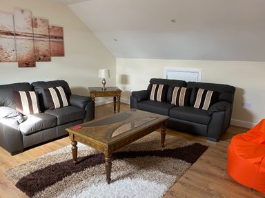 A living room with two sofas, a wooden coffee table, a side table with a lamp, and an orange bean bag at Llygad Yr Haul Sun in Burry Port