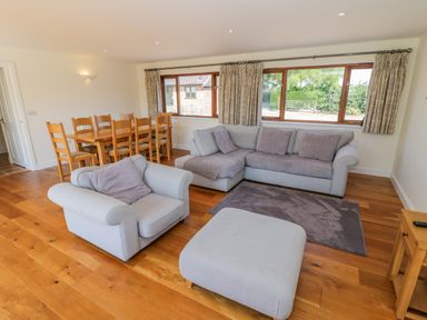 A living room with a grey sofa set and wooden dining table near windows at Little Owl Barn in Upton Snodsbury
