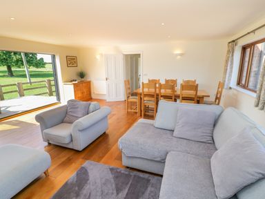 A living room with sofas and a dining table with chairs near a large open door showing a grassy area at Little Owl Barn in Upton Snodsbury