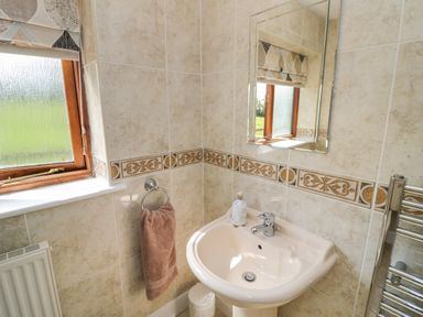 A bathroom sink with a mirror towel ring with a brown towel a window and a radiator at Little Owl Barn in Upton Snodsbury