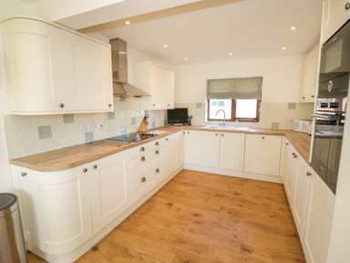 A kitchen with white cabinets a wooden countertop a stovetop a sink and window at Little Owl Barn in Upton Snodsbury
