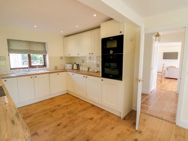 A kitchen with wooden floors white cabinets and a window with a blind at Little Owl Barn in Upton Snodsbury