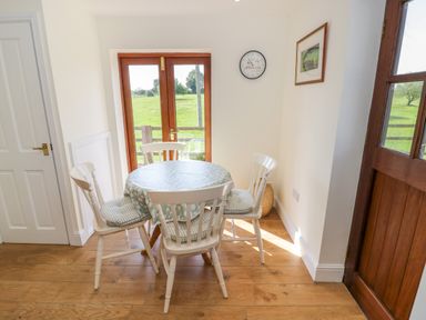 A small dining area with a round table covered with a tablecloth and four chairs near wooden doors at Little Owl Barn in Upton Snodsbury