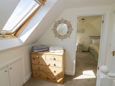 A hallway with a wooden chest of drawers and folded towels under a skylight window leading to a bedroom with a bed and nightstand at Little Owl Barn in Upton Snodsbury