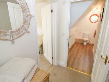 A hallway with two open doors showing a bedroom on the left and a bathroom with a toilet on the right with a round window at Little Owl Barn in Upton Snodsbury