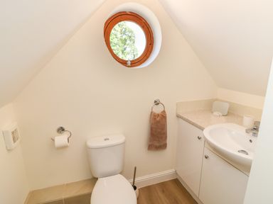 A small bathroom with a toilet a sink and a round window at Little Owl Barn in Upton Snodsbury