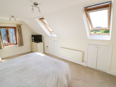 A bedroom with a bed a television on a dresser two windows and two skylights at Little Owl Barn in Upton Snodsbury