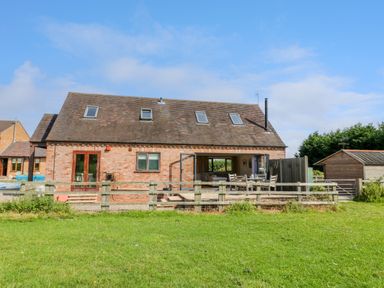 A brick house with a tiled roof and skylights with a fenced yard and patio furniture at Little Owl Barn in Upton Snodsbury