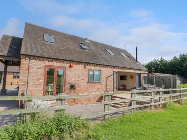 A brick house with skylights and an outdoor seating area behind a wooden fence at Little Owl Barn in Upton Snodsbury