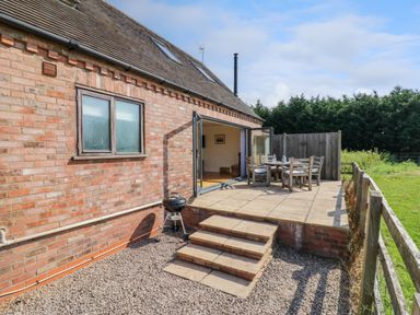 A patio with outdoor dining furniture and a barbecue grill outside a brick house at Little Owl Barn in Upton Snodsbury