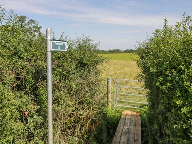 A footpath sign next to a wooden walkway and metal gate leading to a grassy field at Little Owl Barn in Upton Snodsbury