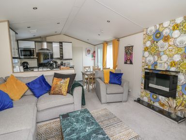 A living room with gray sofas and colorful pillows next to a kitchen and dining table at 95 Hafan Taffy in Gilfachrheda near Llanarth