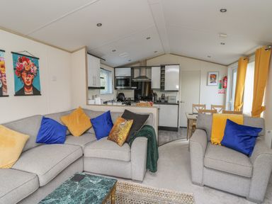 A living area with gray sofas and blue and yellow cushions next to a kitchen and dining table at 95 Hafan Taffy in Gilfachrheda near Llanarth