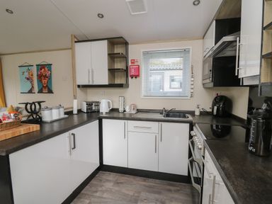 A kitchen with white cabinets black countertops a sink a stove a toaster a kettle and a window at 95 Hafan Taffy in Gilfachrheda near Llanarth
