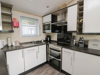 A kitchen with white cabinets a stove a microwave a sink and various kitchen appliances at 95 Hafan Taffy in Gilfachrheda near Llanarth