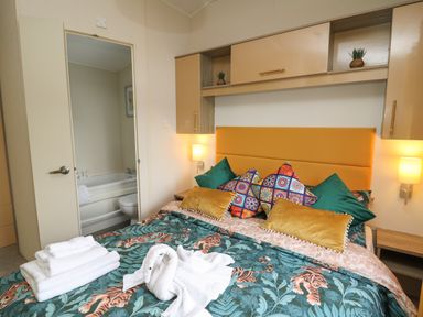 A bedroom with a bed with colorful pillows and a tiger print bedspread and a door open to a bathroom at 95 Hafan Taffy in Gilfachrheda near Llanarth