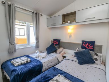 A bedroom with two single beds blue blankets and cushions and grey curtains at 95 Hafan Taffy in Gilfachrheda near Llanarth
