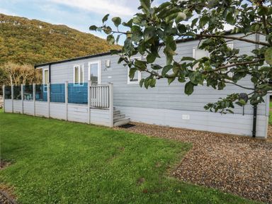 An exterior view of a gray mobile home with small steps leading to a door and a glass panel fence in front at 95 Hafan Taffy in Gilfachrheda near Llanarth