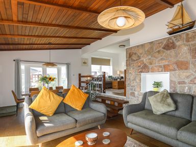 A living room with two gray sofas yellow and gray cushions stone wall and wooden ceiling at Corrie Knowe in Trearddur Bay