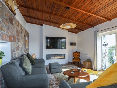 A living room with a stone wall gray sofa wooden coffee table mounted TV and telescope near a window at Corrie Knowe in Trearddur Bay