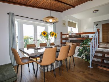 A dining area with a rectangular stone table surrounded by eight brown chairs with sunflowers in a vase on the table at Corrie Knowe in Trearddur Bay