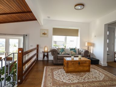 A living room with a brown sofa and wooden chest on a patterned rug at Corrie Knowe in Trearddur Bay
