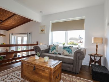 A living area with a grey sofa with sea-themed cushions a wooden chest used as a coffee table and a side table with a lamp at Corrie Knowe in Trearddur Bay