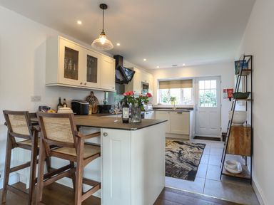 A kitchen with a countertop and two wooden chairs a window and door at Corrie Knowe in Trearddur Bay