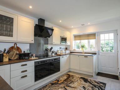 A kitchen with white cabinets black appliances wooden countertop and a patterned rug at Corrie Knowe in Trearddur Bay