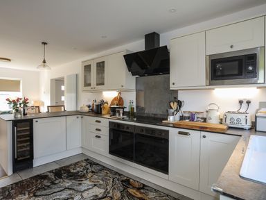 A kitchen with white cabinets black countertop built in oven microwave and wine cooler at Corrie Knowe in Trearddur Bay