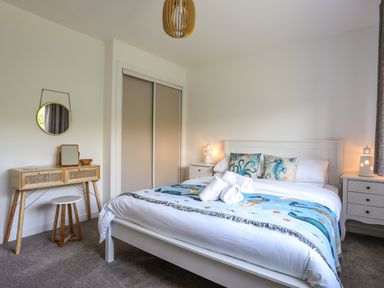 A bedroom with a white bed and blue ocean themed pillows with rolled towels on the bed at Corrie Knowe in Trearddur Bay