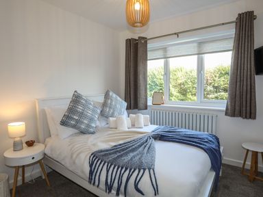 A bedroom with a bed made with pillows and blankets beside a window with curtains at Corrie Knowe in Trearddur Bay