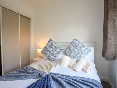 A bedroom with a bed featuring two large cushions and three rolled towels a bedside table with a lamp and sliding wardrobe doors at Corrie Knowe in Trearddur Bay