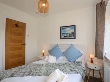 A bedroom with a double bed blue pillows bedside tables lamps and a wooden door at Corrie Knowe in Trearddur Bay