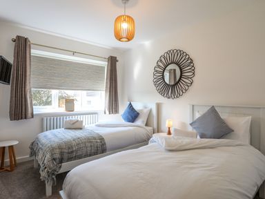 A bedroom with two single beds a round wall mirror and a window with curtains at Corrie Knowe in Trearddur Bay