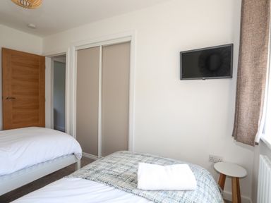 A bedroom with two beds a wall mounted television and a small round table at Corrie Knowe in Trearddur Bay