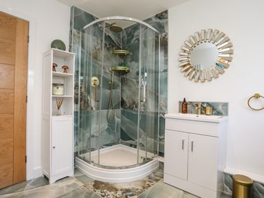 A bathroom with a corner glass shower enclosure a white cabinet a round mirror and a vanity unit at Corrie Knowe in Trearddur Bay