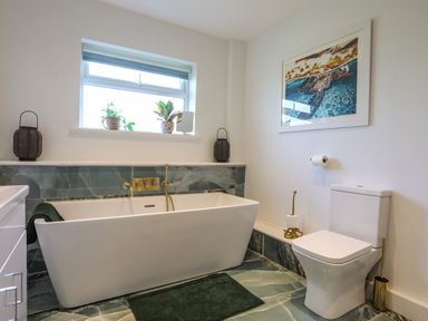 A bathroom with a freestanding bathtub a toilet green floor tiles and plants on the window ledge at Corrie Knowe in Trearddur Bay