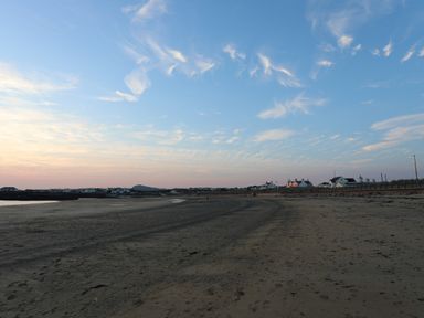 A sandy beach with footprints and distant houses under a blue sky at Corrie Knowe in Trearddur Bay