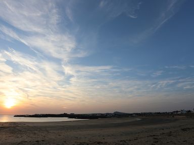A beach with sand and water at sunset with houses and hills in the distance at Corrie Knowe in Trearddur Bay