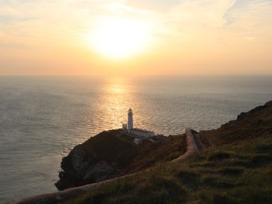 A lighthouse on a cliff overlooking the ocean at sunset at Corrie Knowe in Trearddur Bay