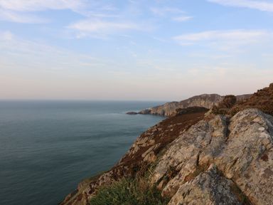 A coastal cliff overlooking the sea with rocky terrain and vegetation at Corrie Knowe in Trearddur Bay